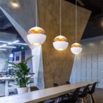 Three white and cork open sphere pendants at different heights above a wood table