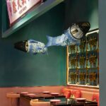 Two fish-shaped lamps hanging above a restaurant booth with a decorative gold panel