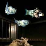 Three fish-shaped fabric pendant lamps painted with scale patterns, lit in a dark setting