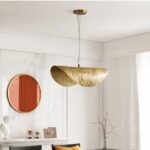 Gold ruffled leaf-shaped pendant light beside a round orange mirror