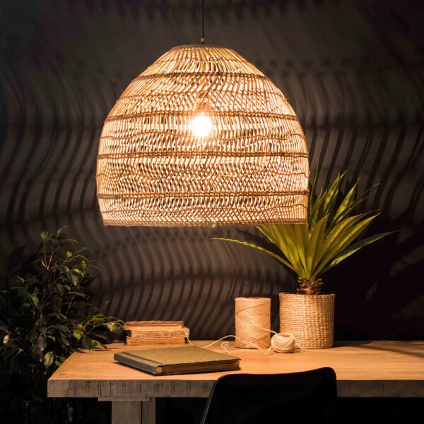 Woven rattan dome pendant light glowing warmly over a wooden desk