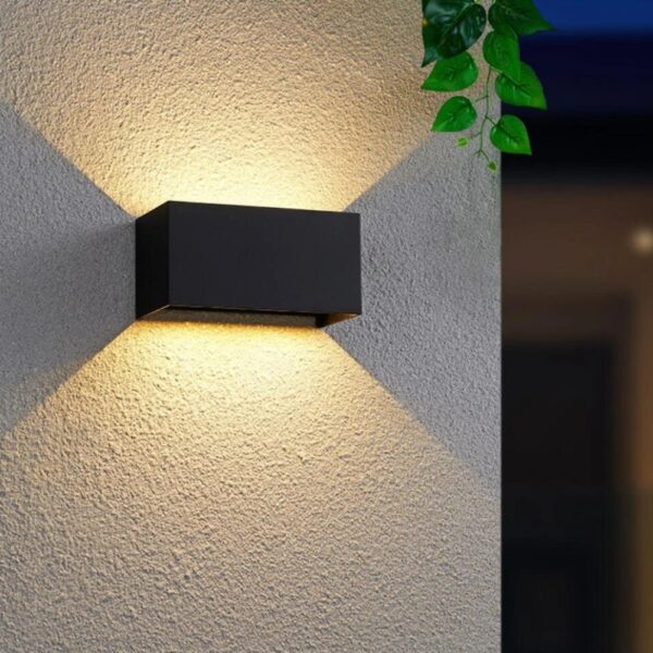Black rectangular outdoor wall light casting light upward and downward on a textured wall