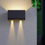 Black rectangular outdoor LED wall light casting light up and down beside leaves