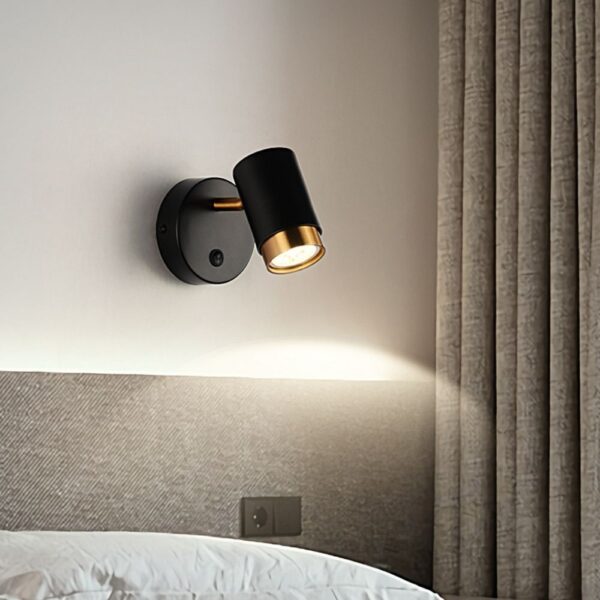 Black adjustable spotlight wall lamp with a brass accent above a bed