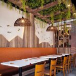Two dark woven dome pendants hanging under a leafy pergola above restaurant booths